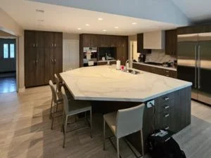 Angular kitchen island with white quartz countertop, dark wood flat-panel cabinetry, and stainless steel appliances