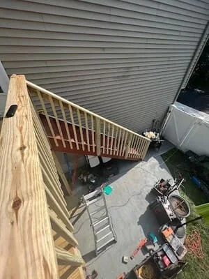 Pressure-treated wood staircase with spaced baluster railing alongside gray vinyl siding and concrete patio
