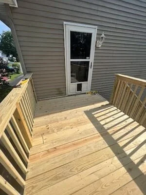 Pressure-treated wood deck with wood railings and balusters leading to a white storm door on gray vinyl siding