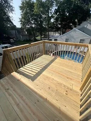 New pressure-treated wood deck with vertical baluster railing and stair stringers overlooking a pool