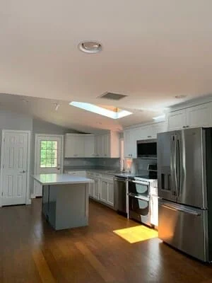 Kitchen with white cabinets, gray island, stainless steel appliances, and skylight in vaulted ceiling