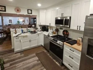 White shaker kitchen cabinets with black pulls, butcher block counters, stainless steel range and microwave, and vinyl plank flooring