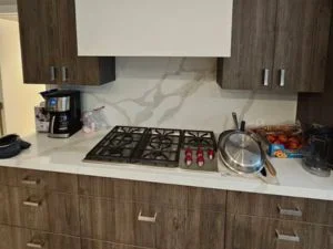 Kitchen with wood-grain flat-panel cabinets, brushed metal pulls, white veined quartz countertop and backsplash, and built-in gas cooktop