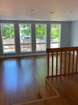 Hardwood floor and stair railing in an open room with four tall white-trimmed windows and gray walls